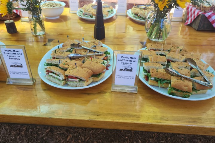 Plates of sandwiches on a wooden table with signs and sunflowers in vases.