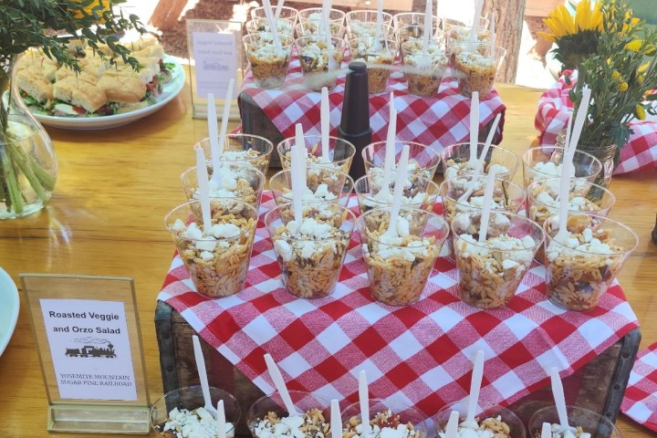 Table with cups of popcorn and salads on a red checkered cloth outdoors.