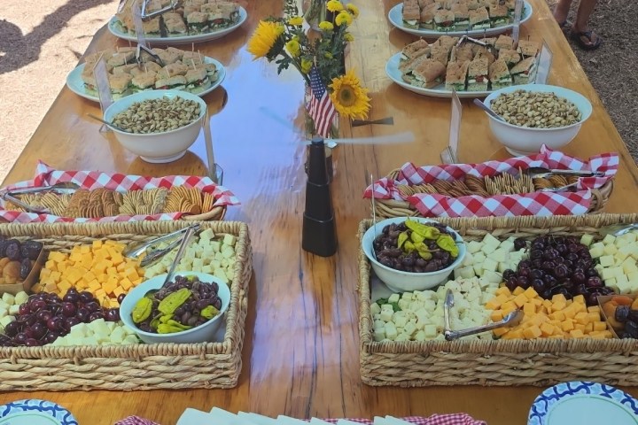 Buffet table with assorted snacks, sunflowers, and checkered cloth outdoors.