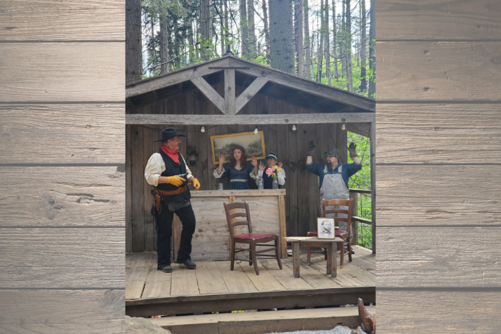 Four people in cowboy attire posing on a wooden stage in a forest setting.